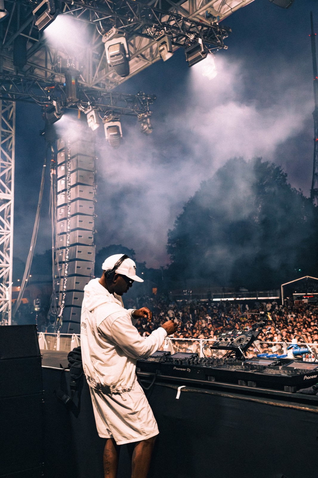 DJ preparing at the decks with the crowd and stage lights behind him.