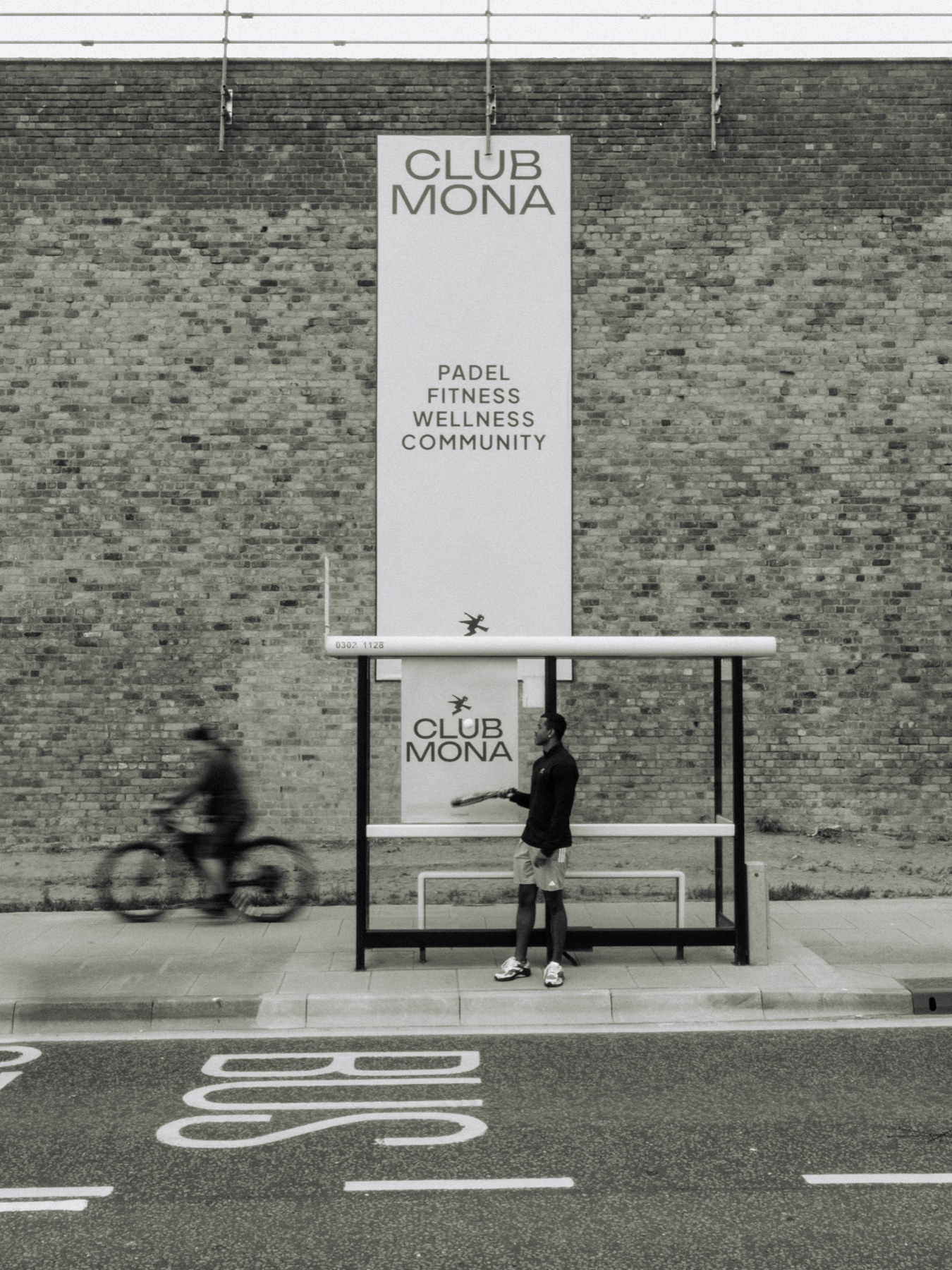 Cyclist passing a Club Mona campaign poster at a bus stop