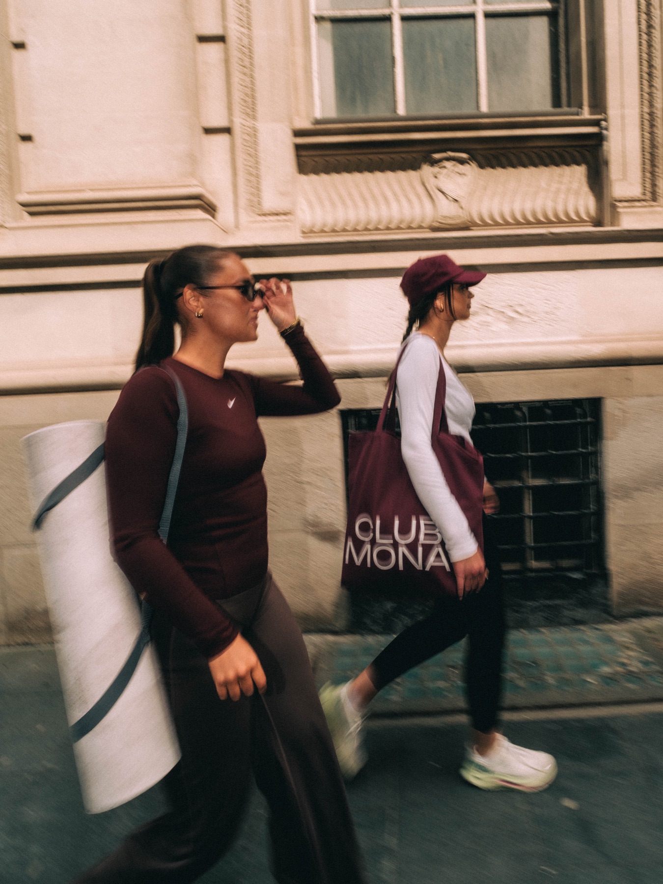 Two women walking beside a Club Mona city poster