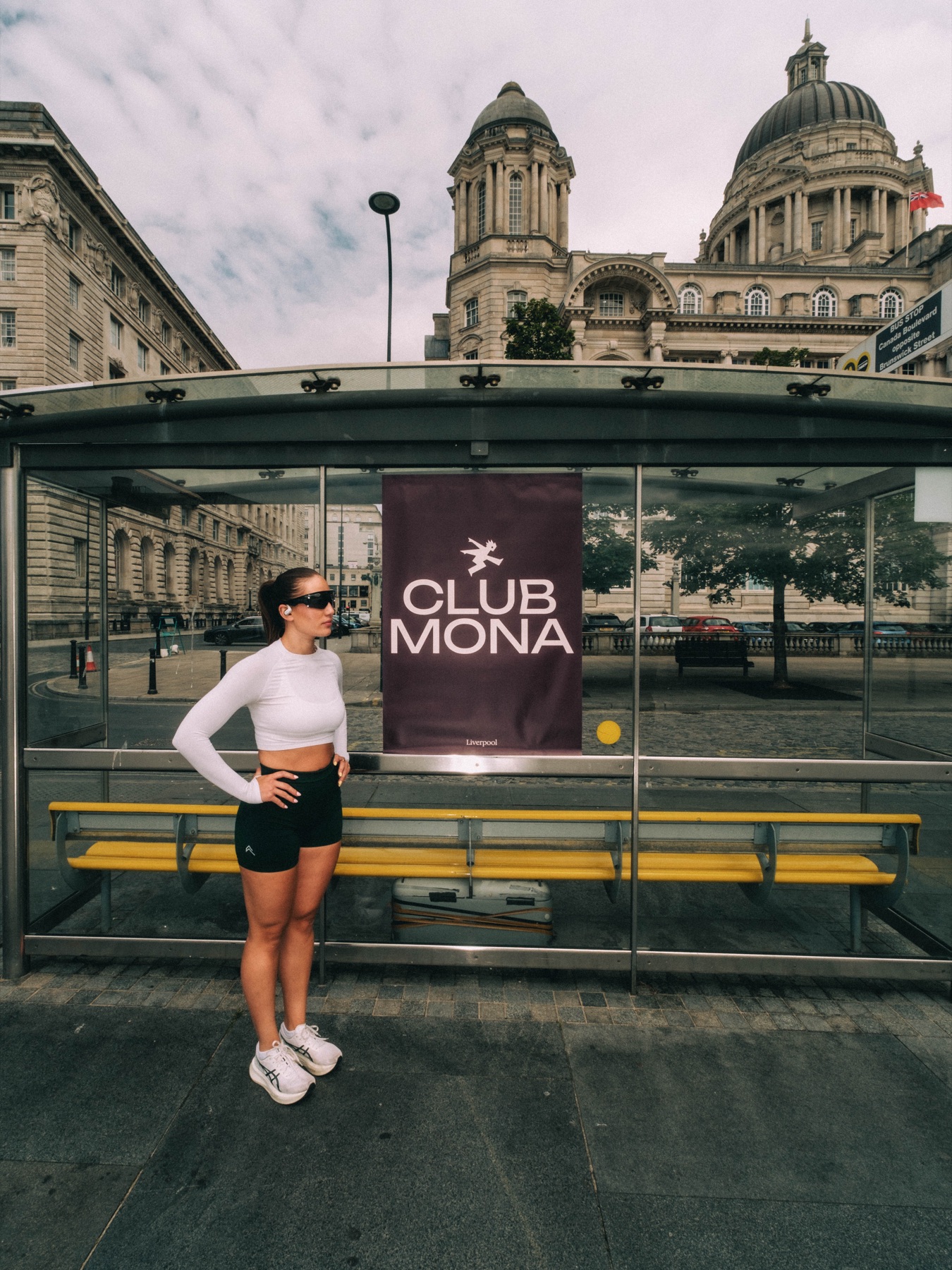 Runner posing beside a Club Mona poster at a bus shelter