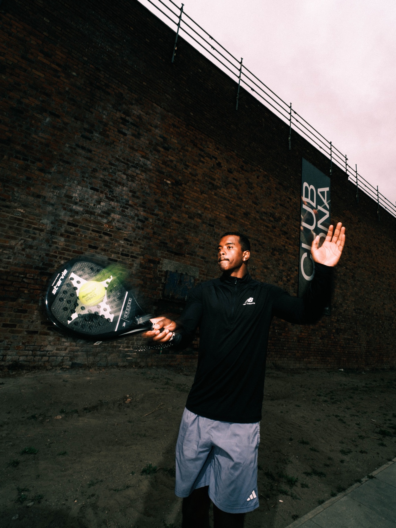 Padel player serving beneath a Club Mona wall poster