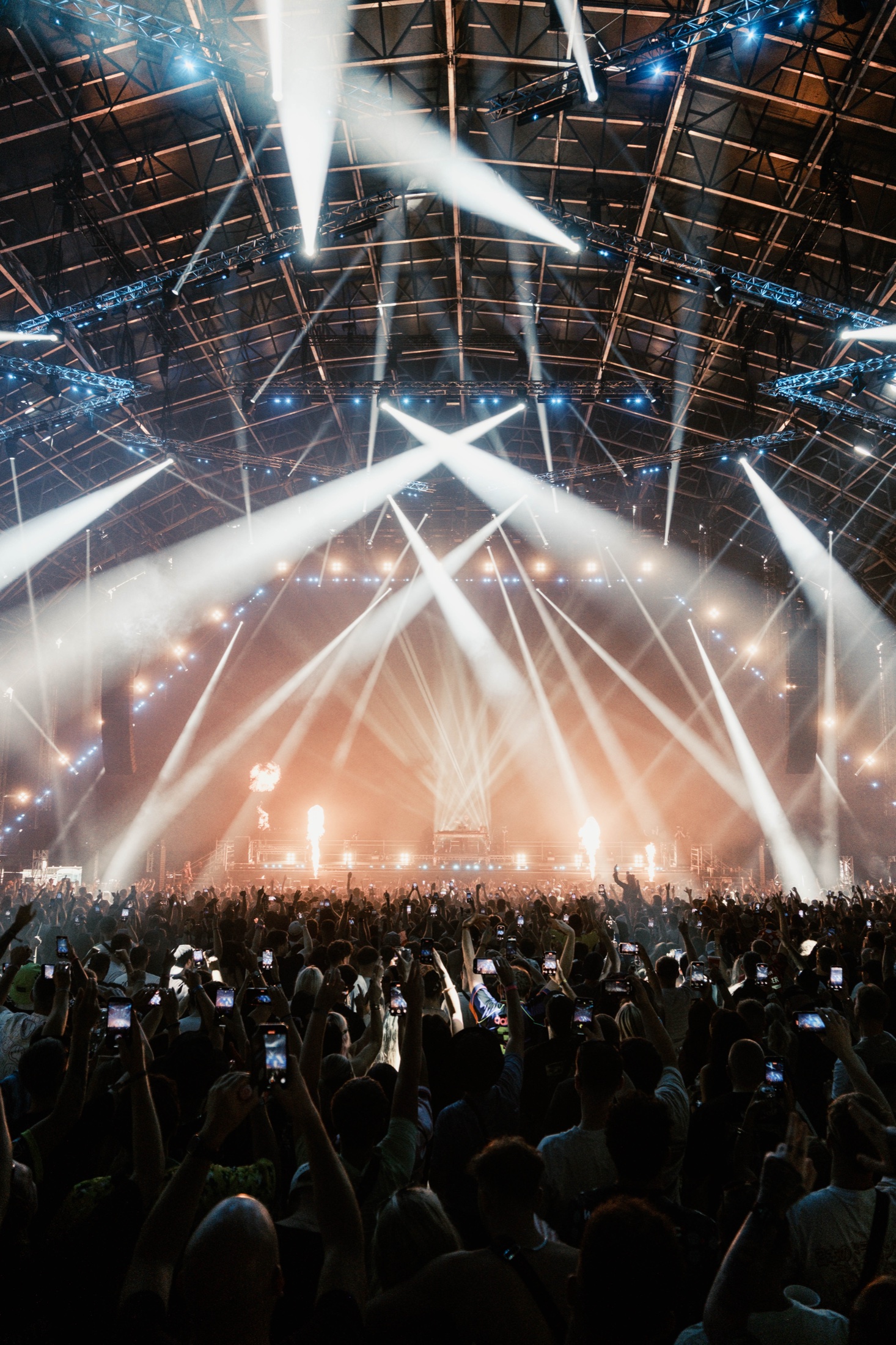 A packed crowd beneath beams of white stage light.