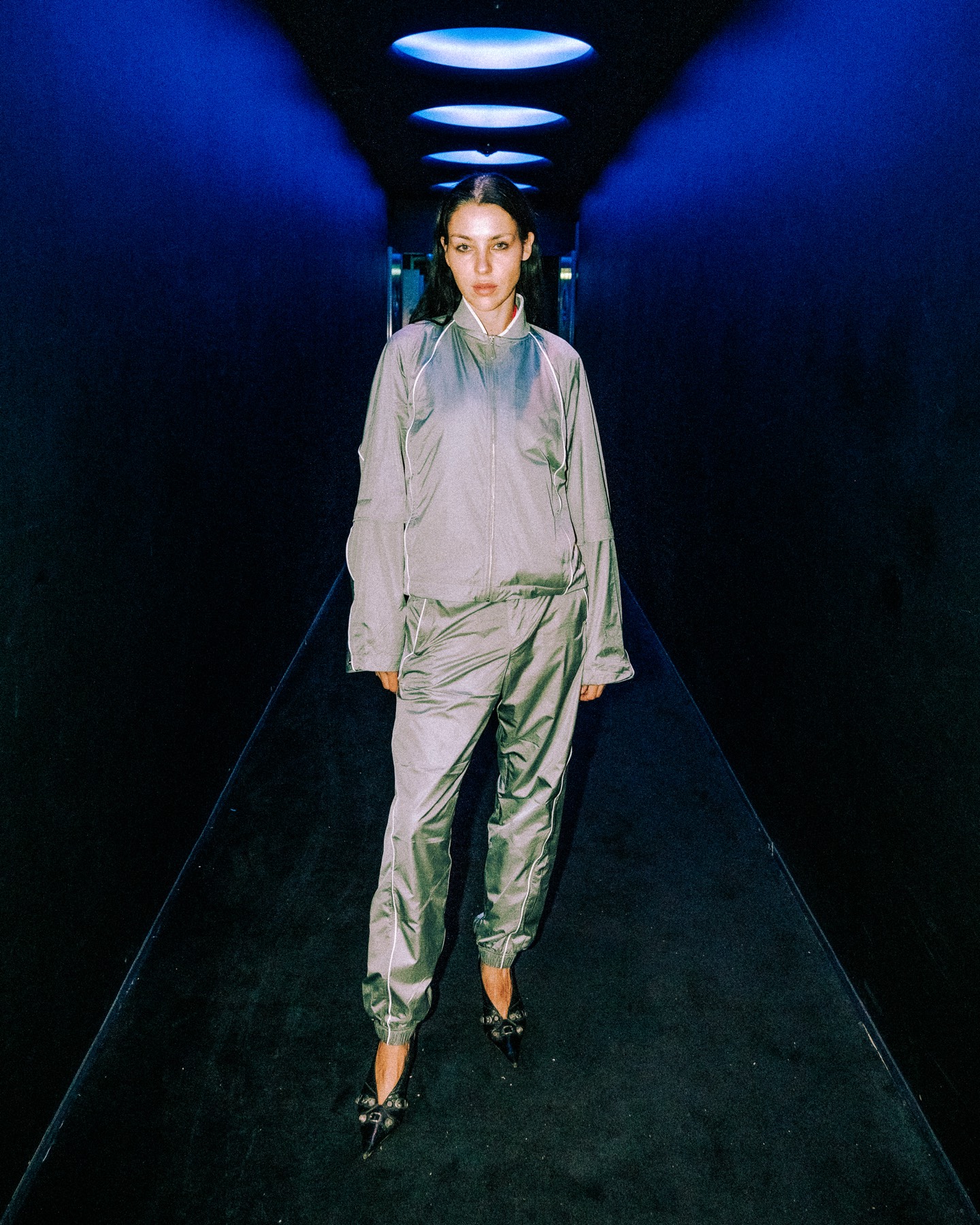 Guest in a silver look photographed in a corridor lit blue.